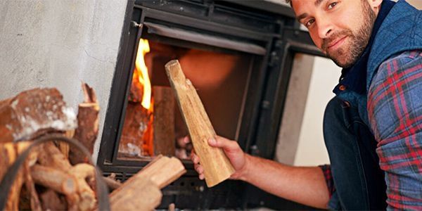Mann steht vor einem Kamin und hält hochwertiges Holz, bereit zum Feuer machen