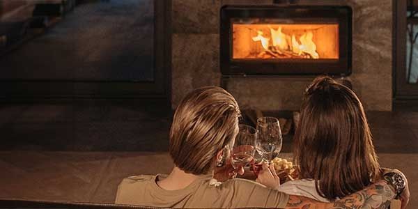 Paar entspannt sich vor einem brennenden Kamin und genießt ein Glas Wein in einem gemütlichen Ambiente